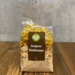 Plastic bag containing Aargauer Rüeblisuppe soup mix with elbow pasta, label shows 'Aargauer Rüeblisuppe' and brand logo on a brown rectangle