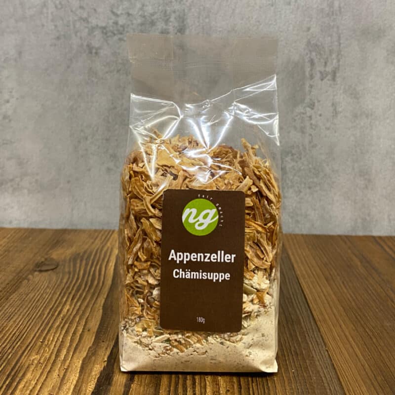 Clear plastic bag containing Appenzeller Chämisuppe dry soup mix on a wooden table; brown label with green logo and 180 g text visible.