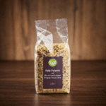 Plastic bag of seasoned red polenta grains with herbs on a wooden surface; label reads 'Rote Polenta mit Marroni und Kräutern, Original Ticino Linie'