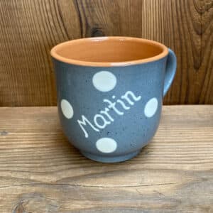 Blue ceramic mug with white polka dots and the name 'Martin' painted on it, sitting on a wooden surface.