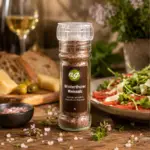 Bottle of Winterthurer Weinsalz pink salt grinder on a rustic table beside bread, cheese, olives, and a salad plate.