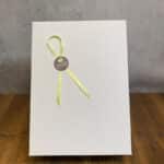 White gift bag with a pale green ribbon loop and a circular NaturGuet tag on the front edge of the bag.
