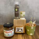 Honey jar labeled Honig on a wooden table beside a decorative ceramic cup and a clear spice grinder atop a wooden block, with a green polka-dot plant pot nearby.