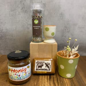 Honey jar labeled Honig on a wooden table beside a decorative ceramic cup and a clear spice grinder atop a wooden block, with a green polka-dot plant pot nearby.