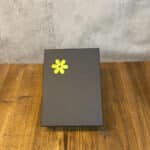 Dark gray gift box with a yellow daisy sticker on a wooden table surface.