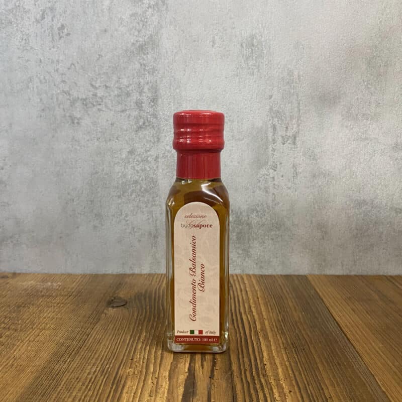 Bottle of Italian balsamic vinegar with a red cap on a wooden surface, label visible in the center of the bottle.