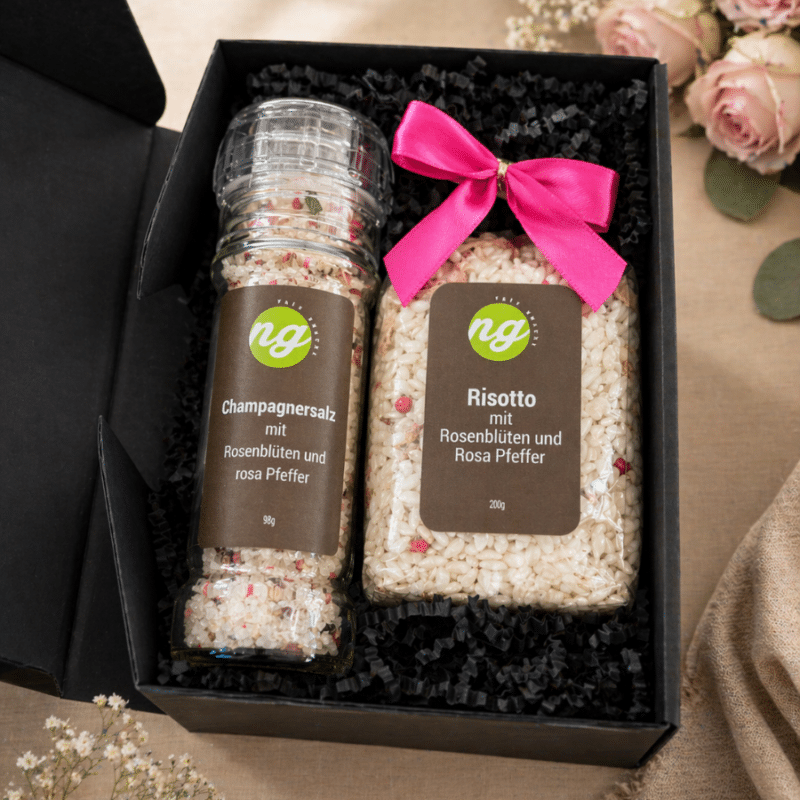 Gift box containing two seasoning jars labeled 'Champagnersalz' and 'Risotto mit Rosenblüten und Rosa Pfeffer' with a pink ribbon.