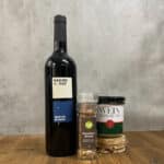 Tall dark wine bottle on a wooden table beside two labeled seasoning jars: Winterthurer Weinsalz and Wein Risotto, with a clear pepper grinder nearby.