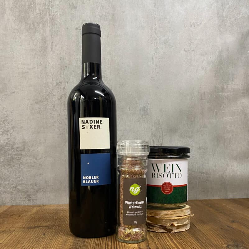 Tall dark wine bottle on a wooden table beside two labeled seasoning jars: Winterthurer Weinsalz and Wein Risotto, with a clear pepper grinder nearby.