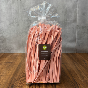 Bag of pink flat pasta ribbons labeled Winterthurer Wein-Nudeln inside a clear gift bag on a wooden table, ready for sale or gift.